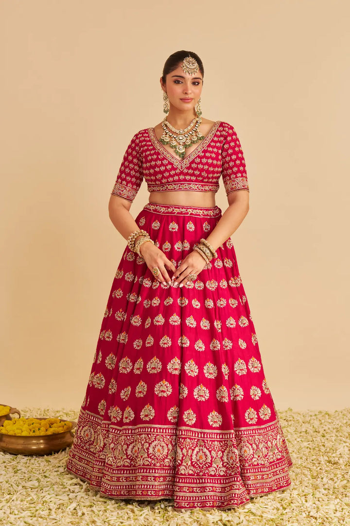 Woman wearing a pink traditional lehenga with gold patterns on a beige background