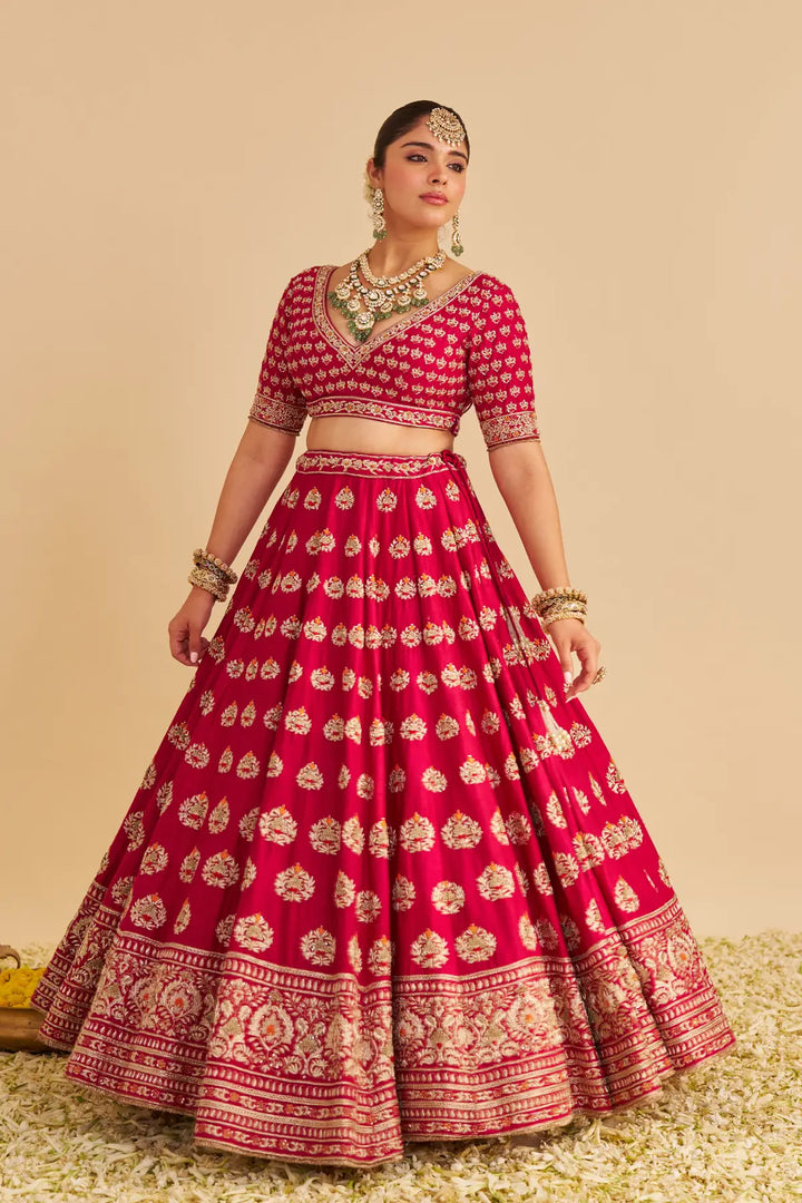 Woman wearing a red and gold traditional lehenga with jewelry against a beige background