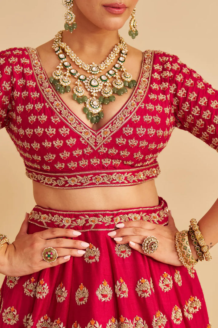 Red embroidered traditional outfit with gold jewelry on a beige background