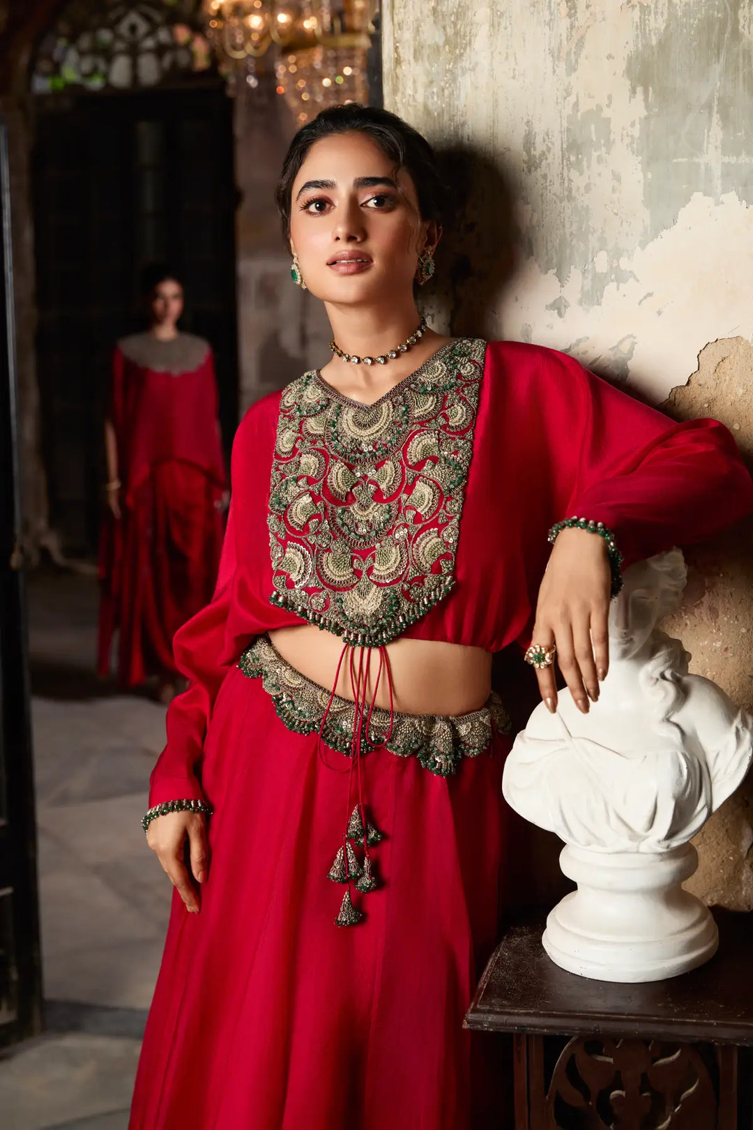 Woman in a red traditional Skirt with intricate patterns, standing in an ornate interior setting.