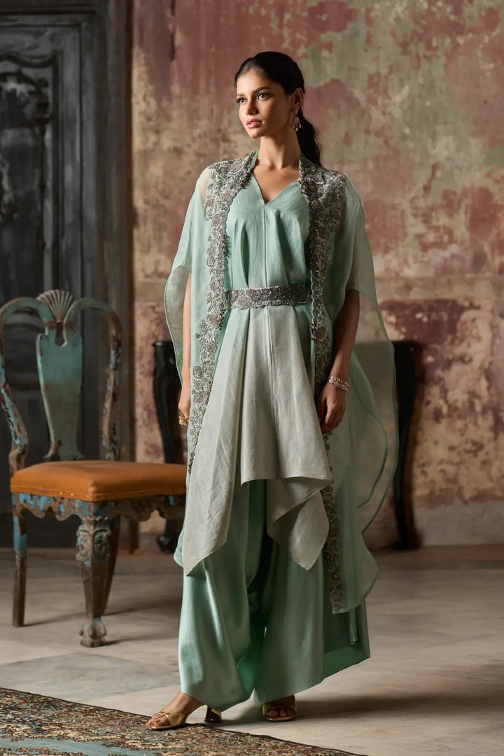Woman in a light green traditional cape set standing in an ornate room.