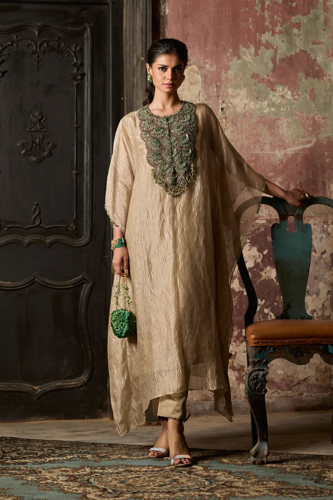 Woman in a beige traditional kaftan with intricate detailing standing in an ornate room.