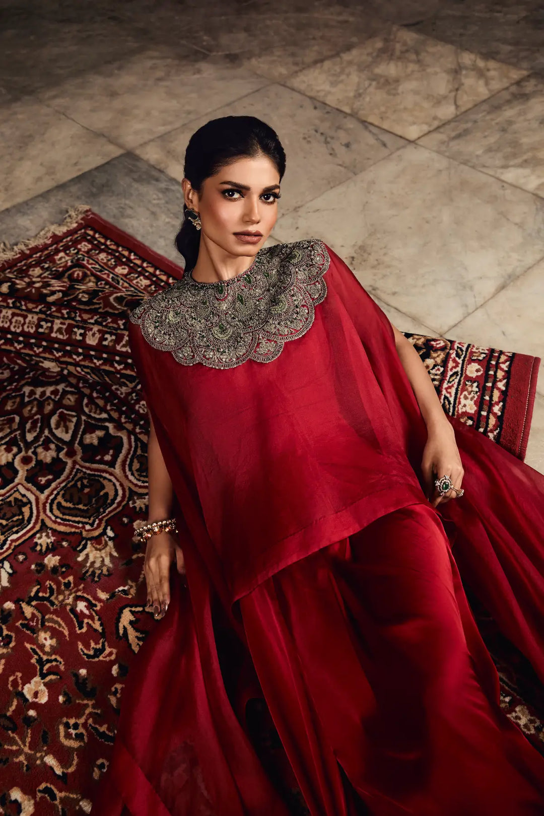 Woman in a red traditional kaftan with intricate detailing, sitting on a patterned rug.