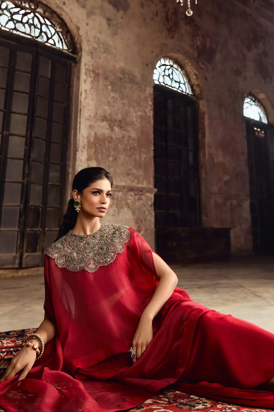 Woman in a red kaftan with intricate detailing sitting in an ornate room.