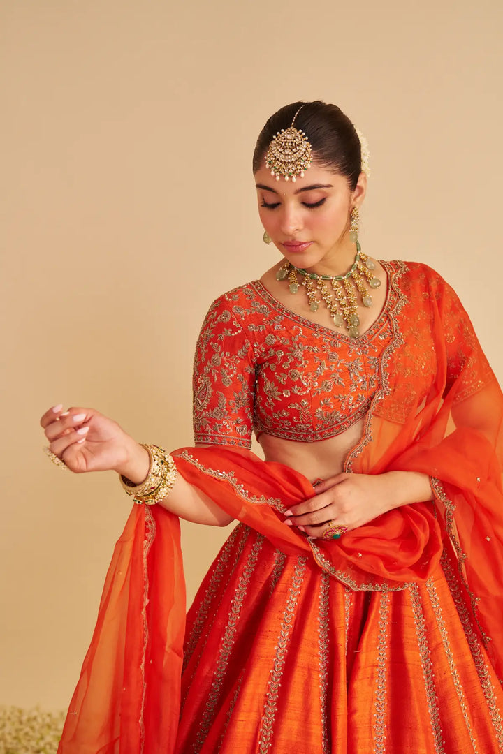 Woman in traditional orange embroidered lehenga with jewelry against a beige background