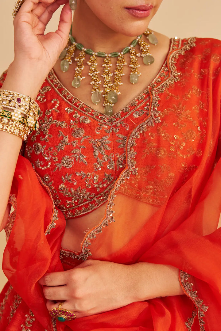 Red embroidered traditional lehenga with gold detailing on a beige background