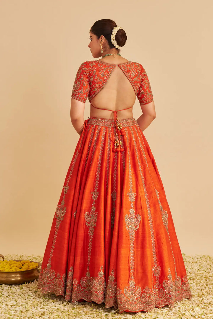 Woman wearing a red embroidered traditional lehenga on a beige background