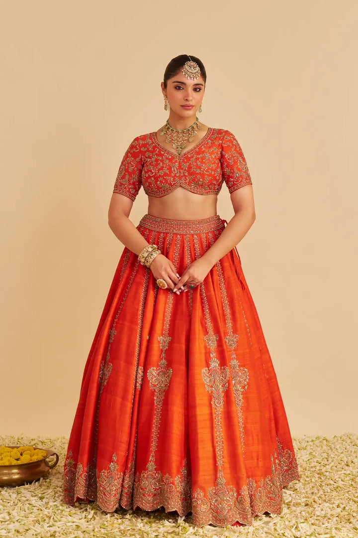 Woman wearing an orange traditional lehenga with intricate designs on a beige background