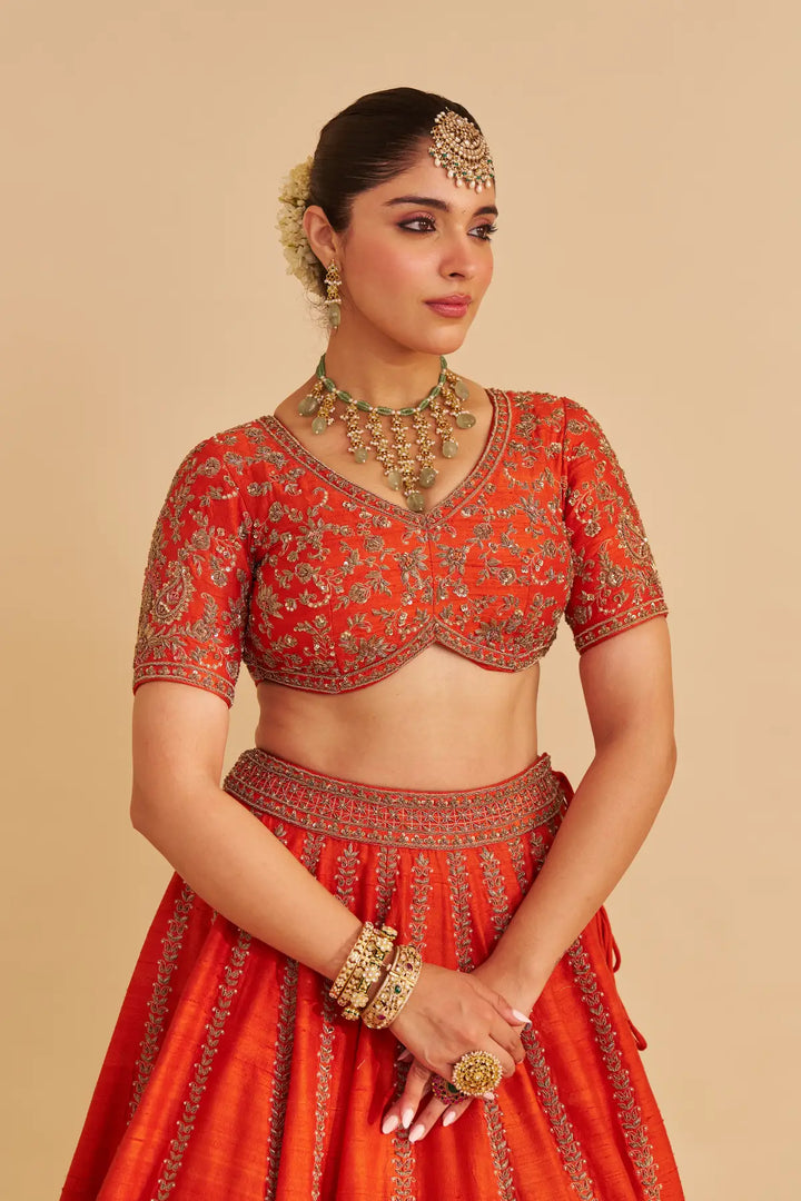 Woman wearing a red embroidered traditional lehenga with jewellery on a beige background