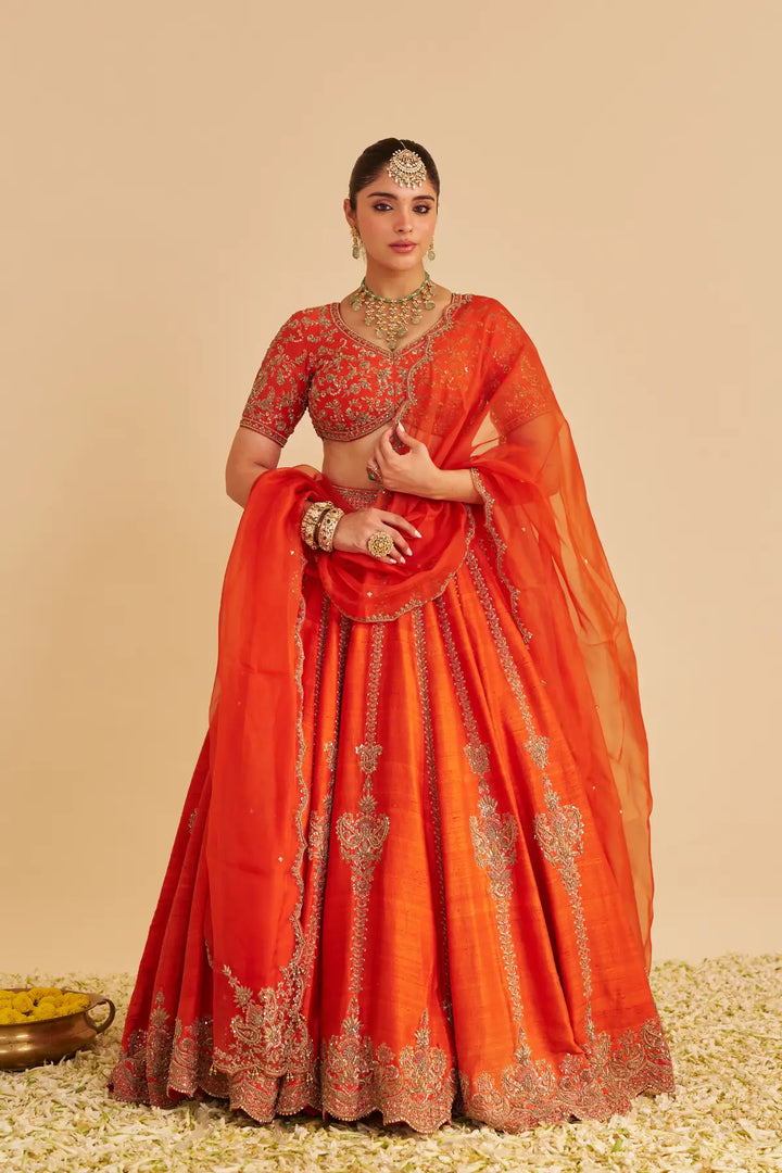 Woman wearing a traditional orange lehenga with intricate patterns on a beige background