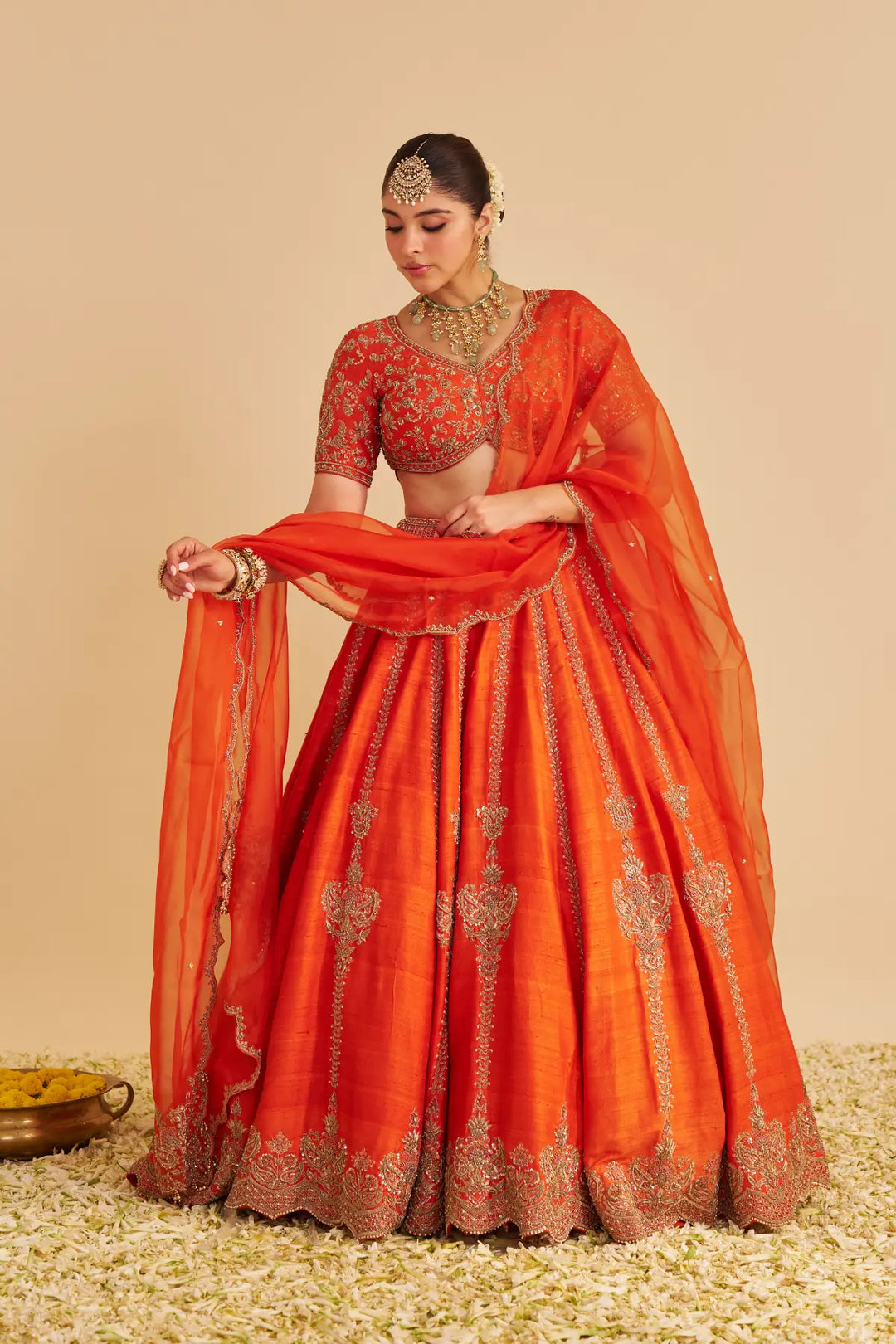 Woman in traditional orange lehenga with intricate patterns on a beige background