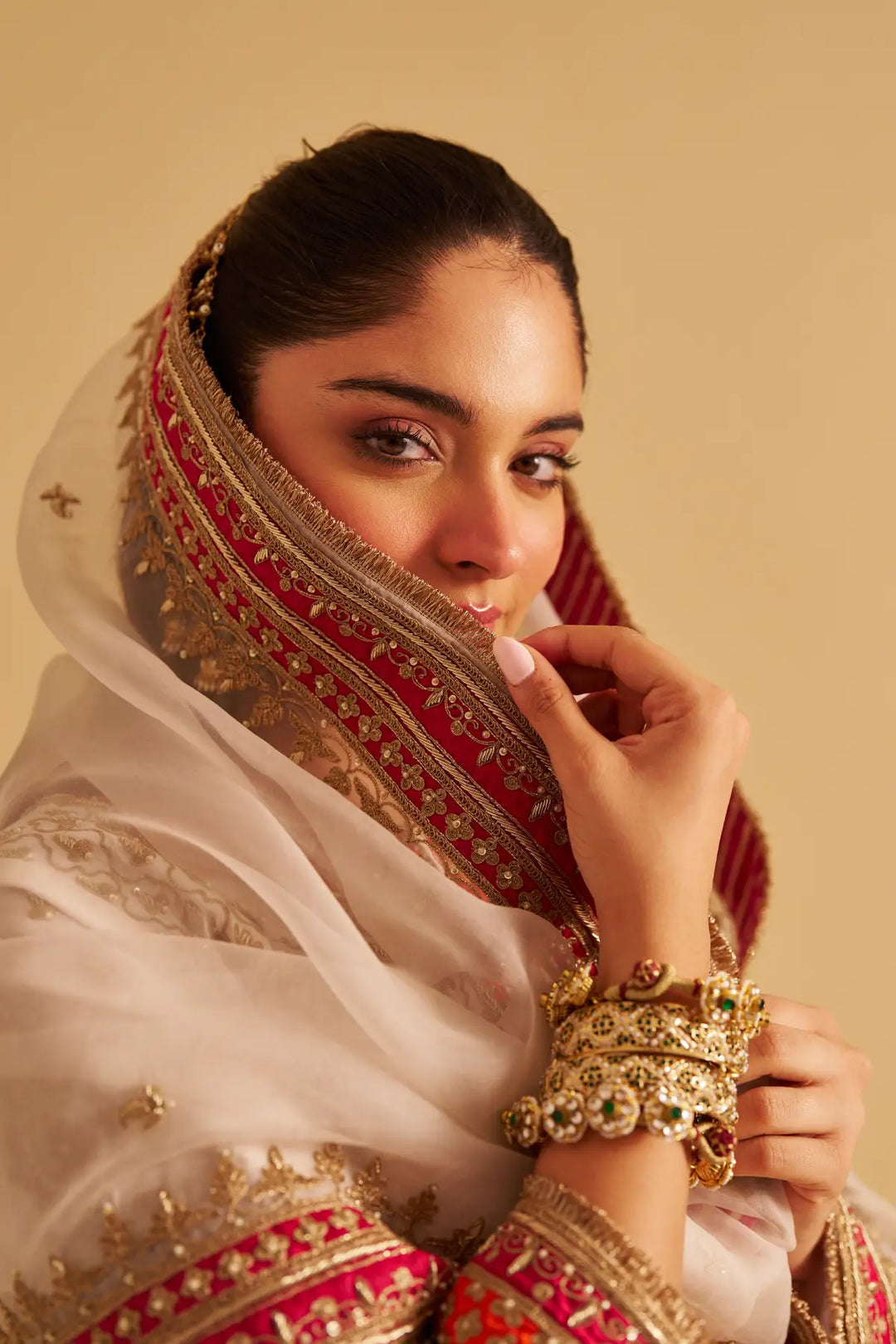 Woman wearing a traditional embroidered outfit with gold jewelry against a beige background
