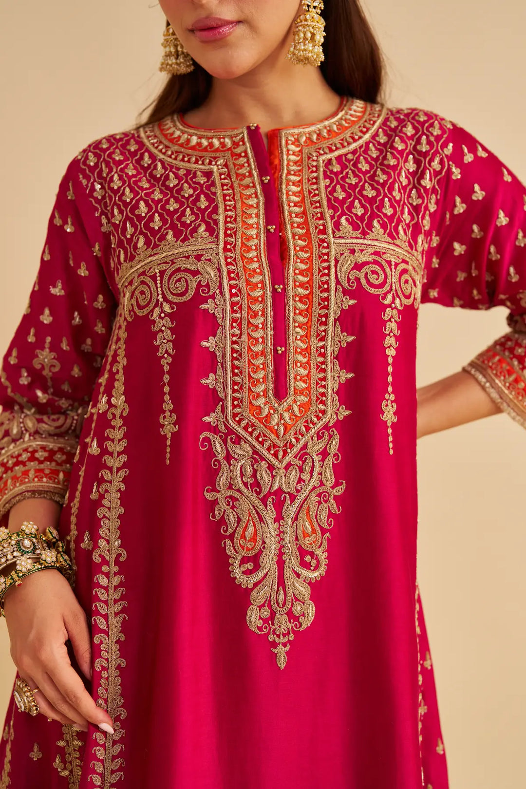 Red embroidered traditional outfit with gold details on a beige background