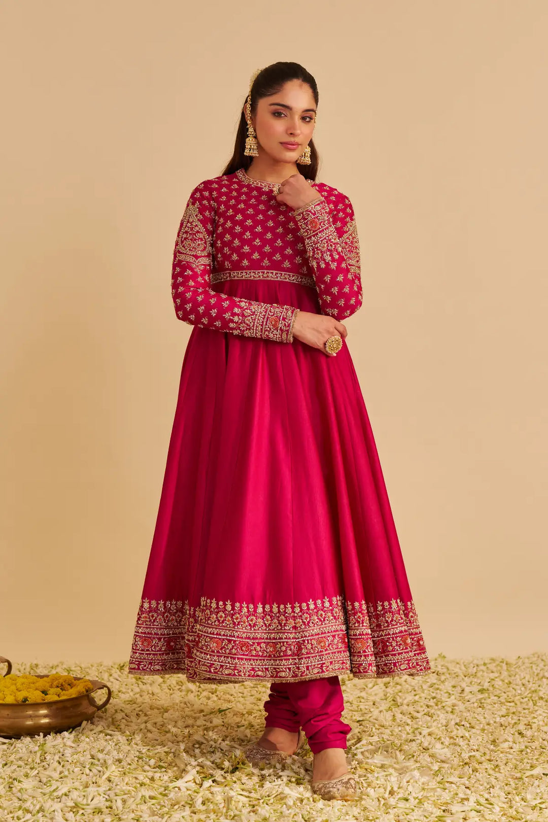 Woman wearing a pink traditional Anarkali with intricate patterns on a beige background
