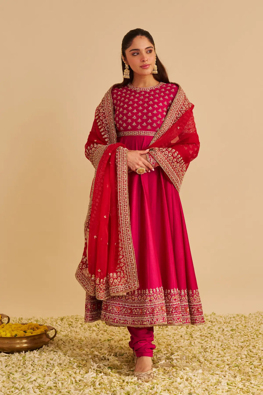 Woman wearing a red traditional Anarkali with gold embroidery on a beige background