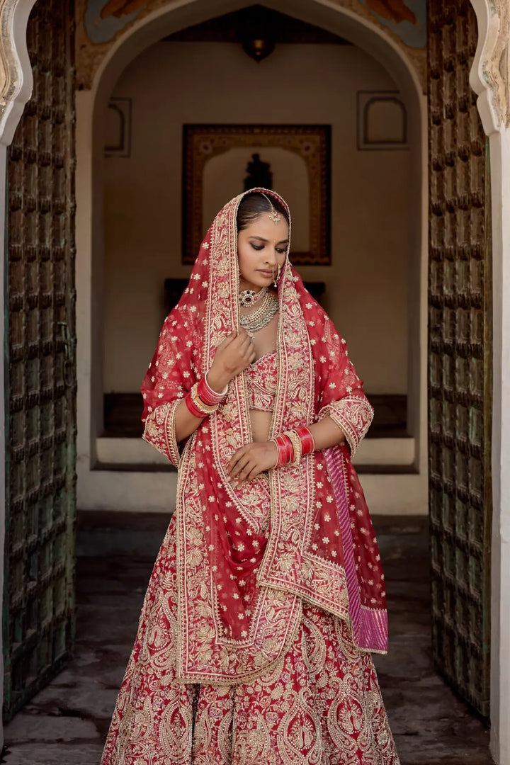 Woman in traditional red and gold bridal outfit standing in an archway.