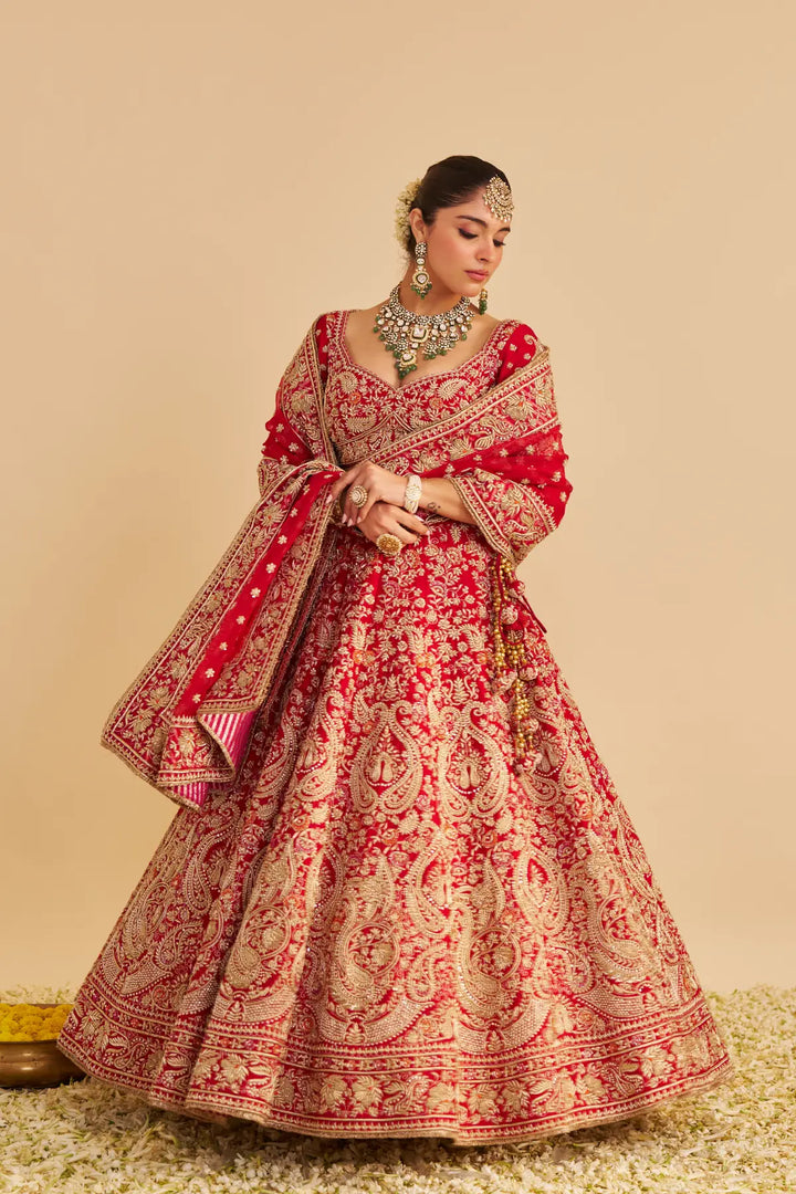 Woman wearing a traditional red and gold embroidered lehenga on a beige background