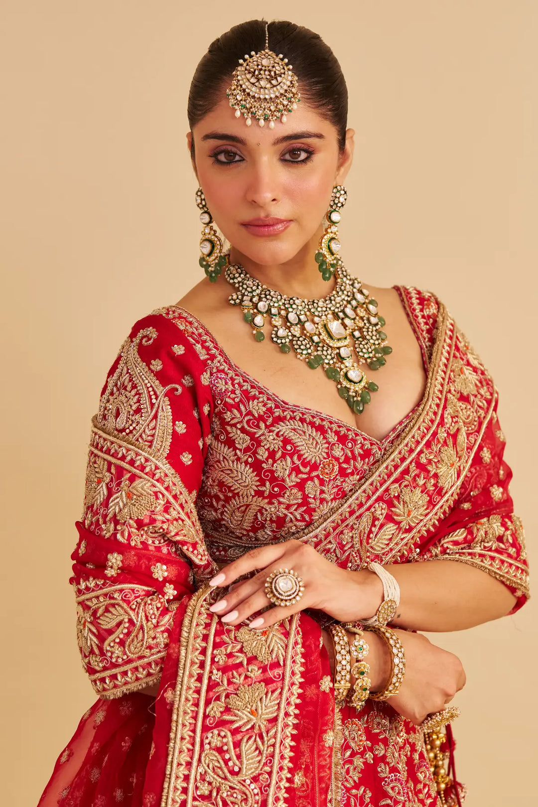 Woman in traditional red and gold embroidered outfit with jewelry on a beige background