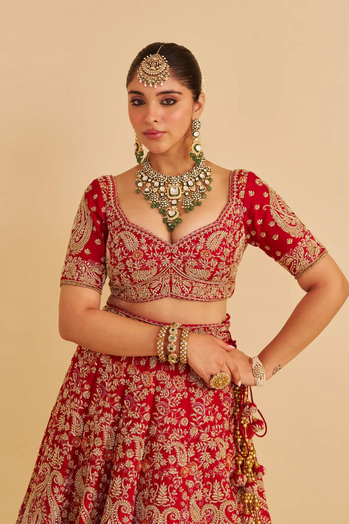 Woman wearing a red and gold traditional outfit with jewelry on a beige background