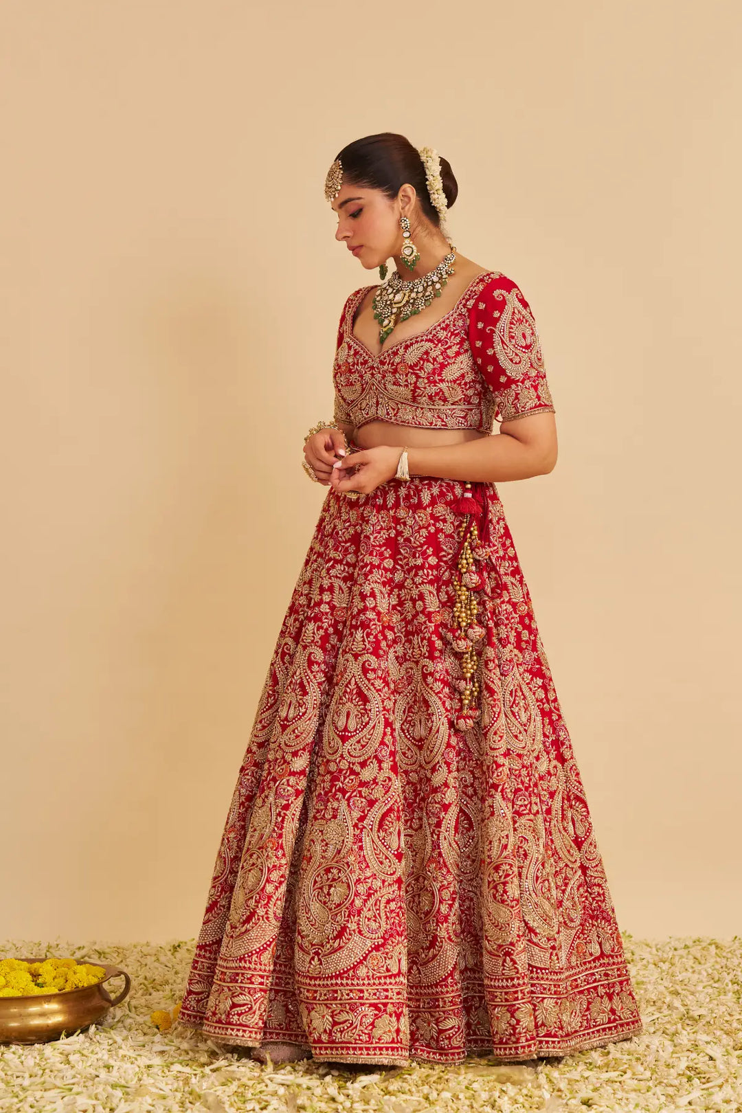 Woman wearing a red and gold embroidered traditional lehenga on a beige background