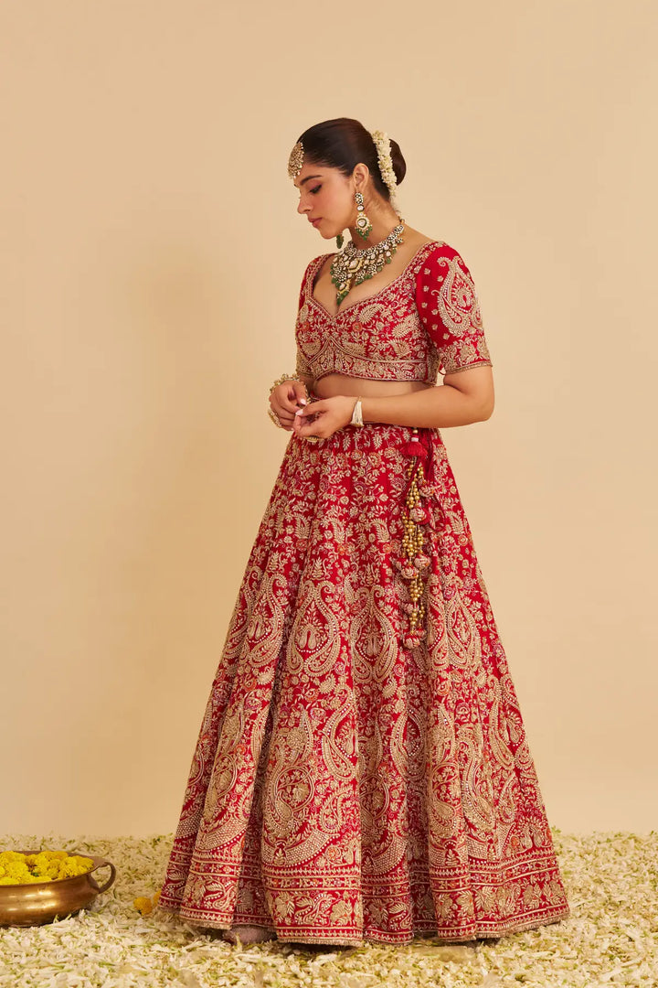Woman wearing a red and gold embroidered traditional lehenga on a beige background