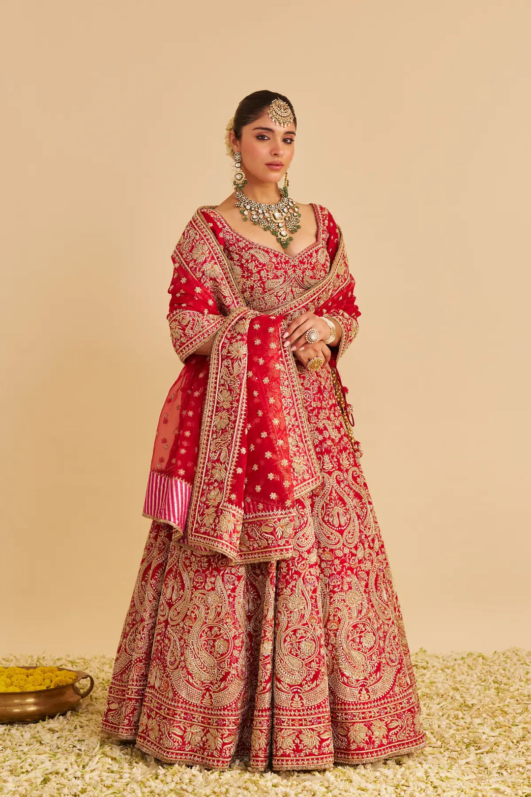Woman in a red and gold traditional lehenga with jewelry against a beige background
