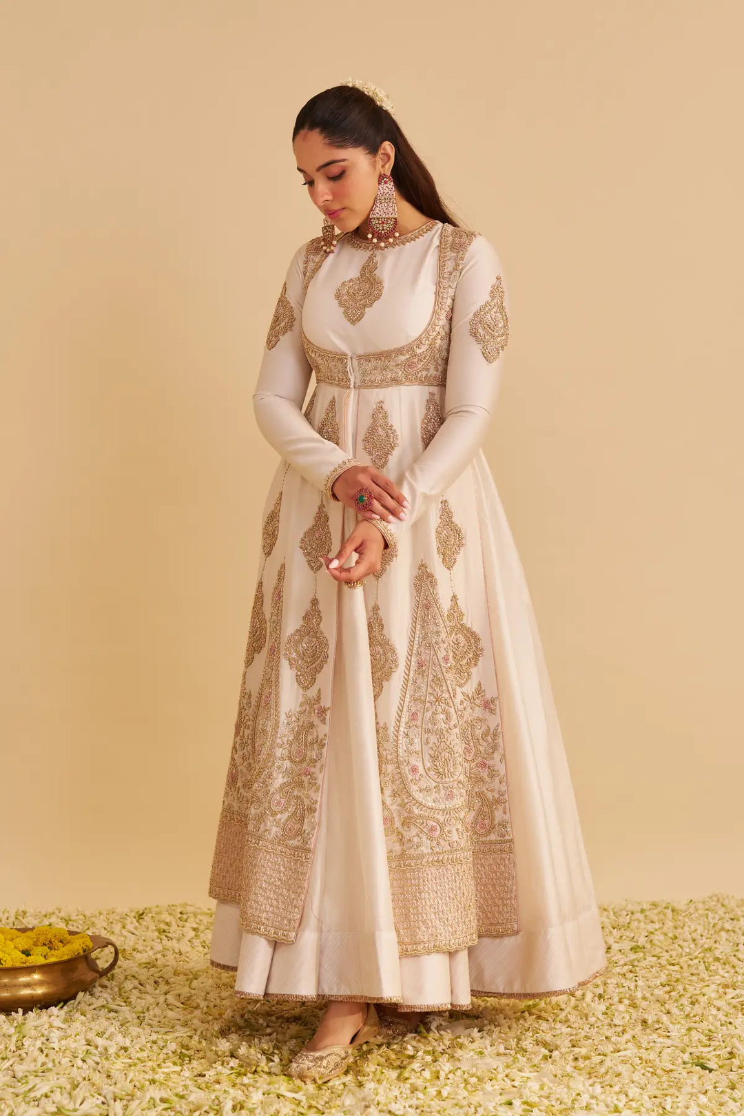 Woman wearing a white and gold embroidered traditional anarkali on a beige background