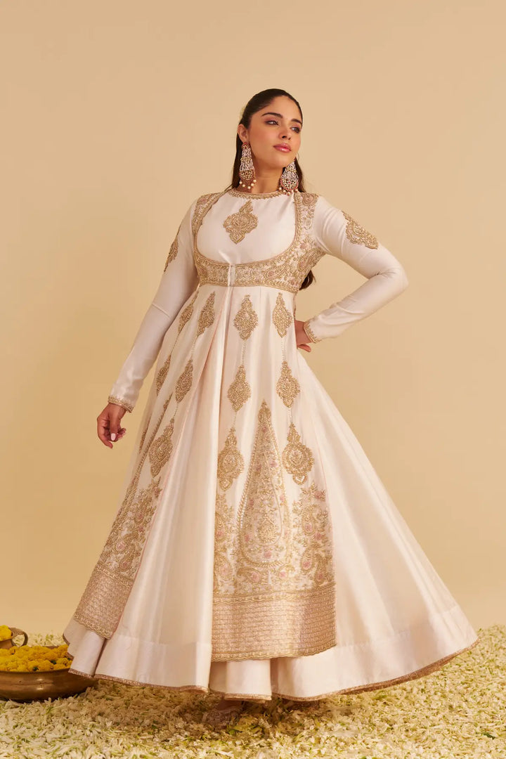 Woman wearing a white and gold embroidered traditional anarkali on a beige background