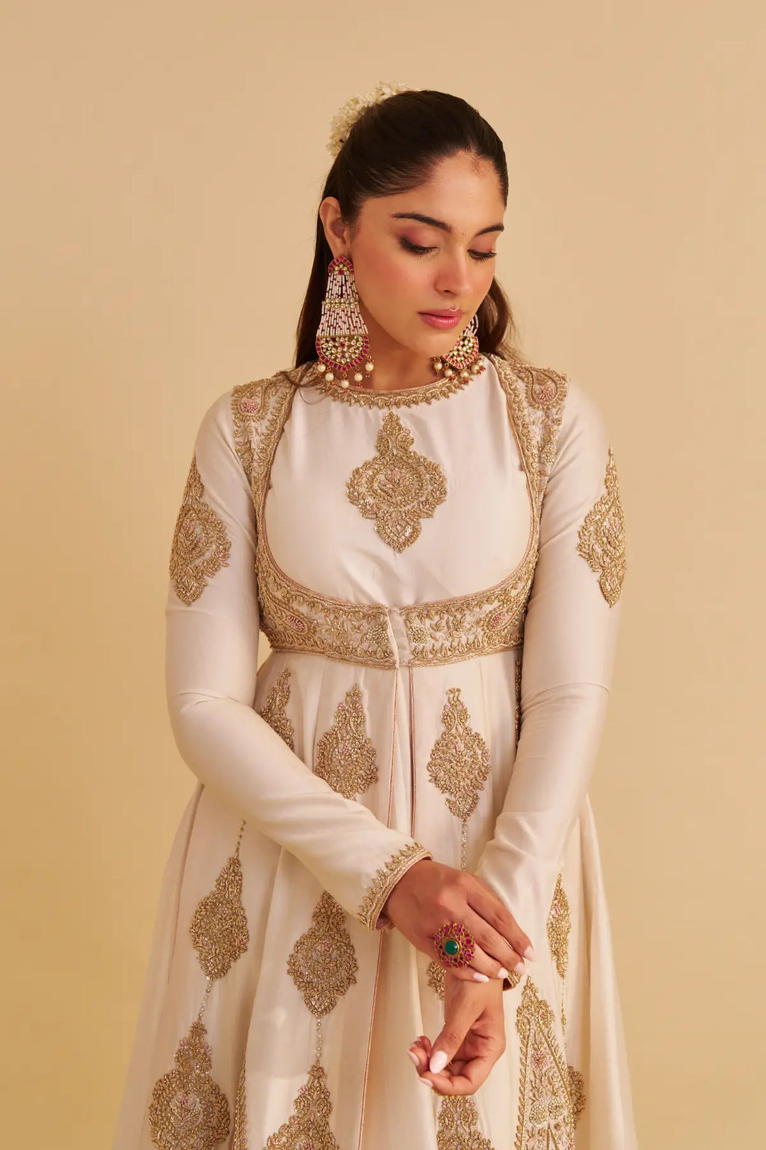 Woman wearing a white traditional anarkali with gold embroidery on a beige background