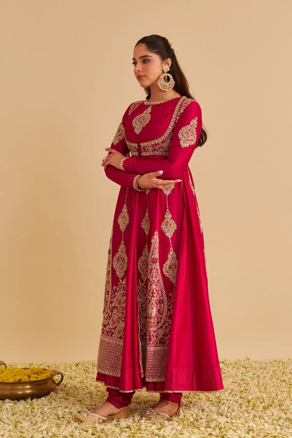 Woman in a red traditional anarkali with gold embroidery on a beige background