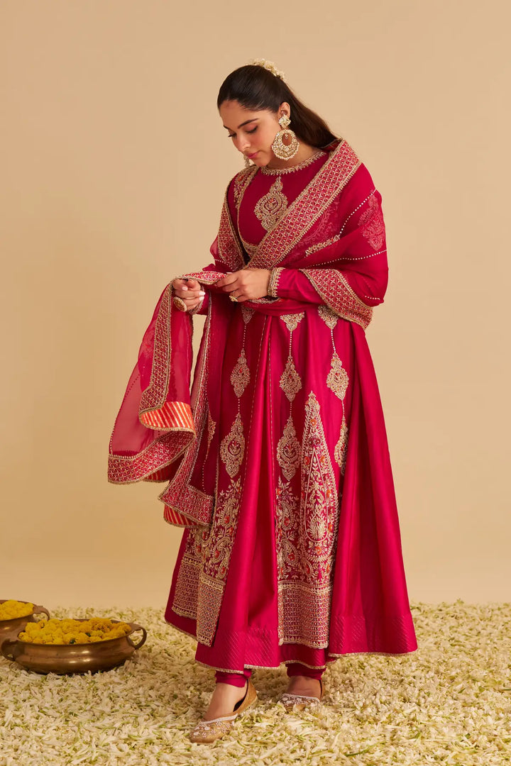 Woman in a traditional red and gold anarkali with a matching shawl on a beige background